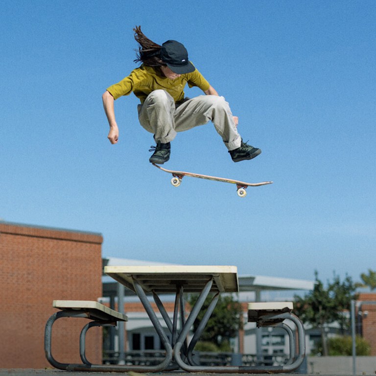 Two images of Vans Skate Team Rider Shiloh Catori wearing the Skate Old Skool™ 36+ by Atiba for Vans jumping over a table and leaning on a fence.