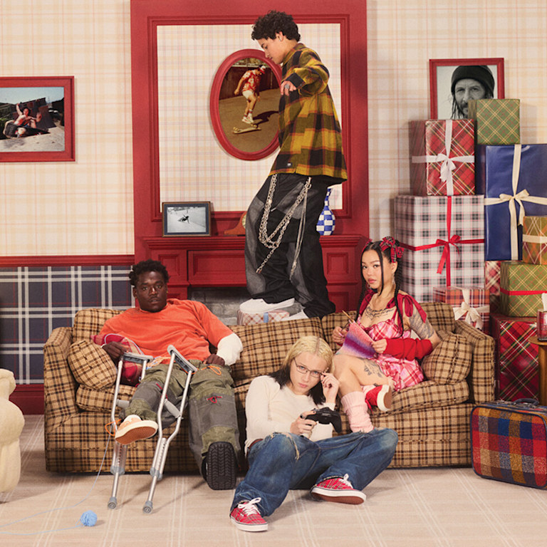  Un groupe éclectique de planchistes, d’influenceurs et de musiciens est assis sur un vieux sofa sur le plateau d’une sitcom, entouré de cadeaux.