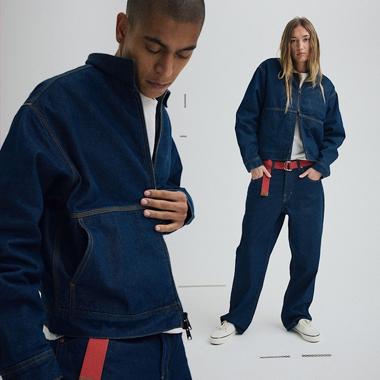 Man and woman standing in a grey photography studio. Both are wearing the same Premium Denim Station Jacket.