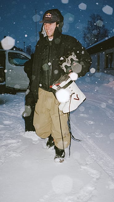 A man walks in the snow with white Vans snowboarding boots.