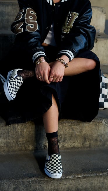 A person sitting with their their legs crossed wearing black and white checkerboard shoes.