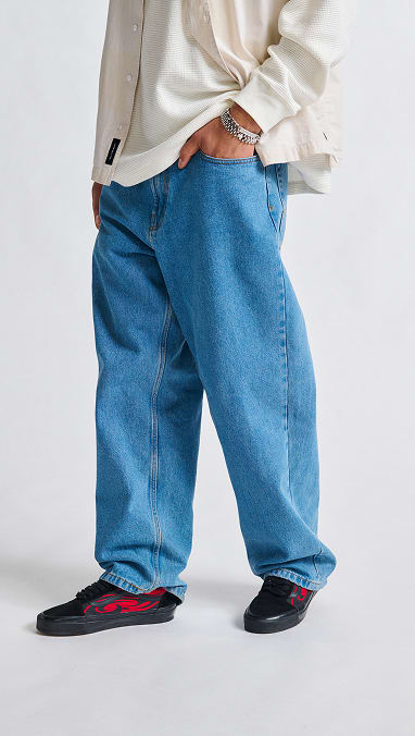A man standing with his hand in the pocket of baggy blue jeans and black and red flame print Premium Old Skool from the Premium Old Skool Music Collection.