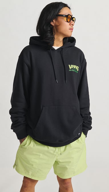A man wearing a Vans black hoodie, Vans sunglasses with yellow lenses, and neon green shorts.