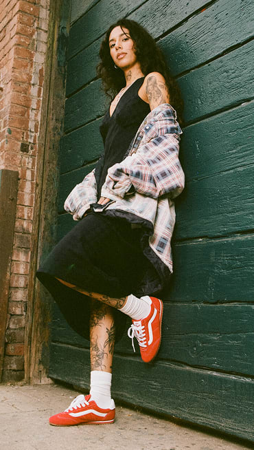 A woman posing against a garage door in red Super Lowpros and a flannel.