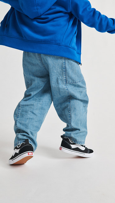 A child in a bright blue hoodie, wearing loose denim jeans and Kids Knu Skool shoes, showcasing a casual and playful style.