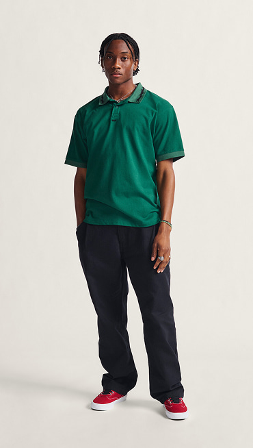 A man posing in a green polo, black jeans, and red Curren shoes.