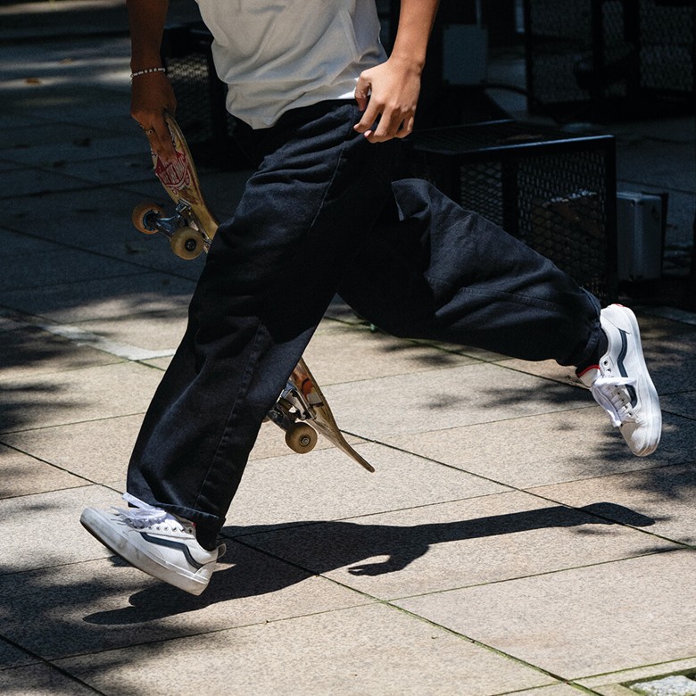 A skater running to get on his board outside on a sidewalk wearing white and black Skate Old Skool.