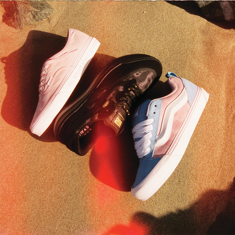 Three pairs of Vans shoes in pink and cyan lay on the sand.