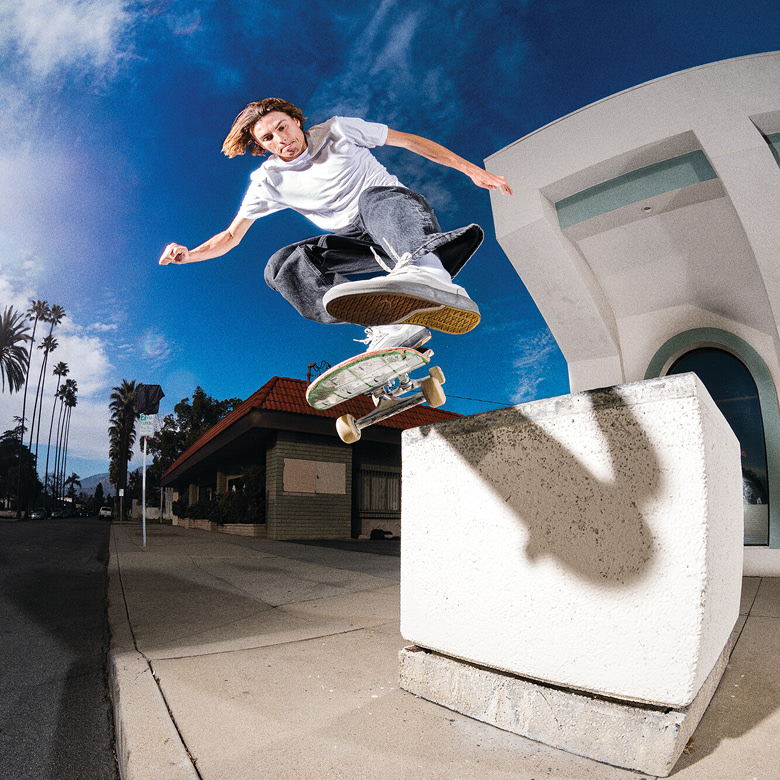 Vans skateboarder Curren Caples does a trick in the air wearing a white t-shirt, black jeans, and white Curren shoes.