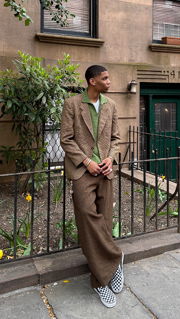 @nassnyc sits on a staircase wearing a brown houndstooth blazer, baggy tweed pants, and white and black Checkerboard Classic Slip-On.