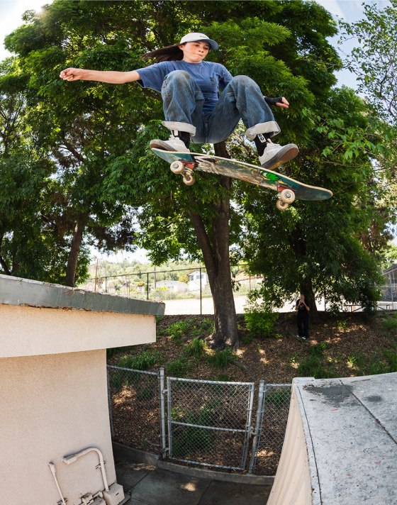 A skater with rolled up jeans climbs a ladder to a roof wearing gray Curren shoes.