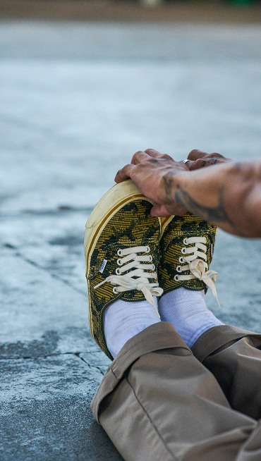 Close-up of a person’s feet as they stretch by pulling at the toes of their Vans Premium Authentic shoes in Antique Gold / Green color.