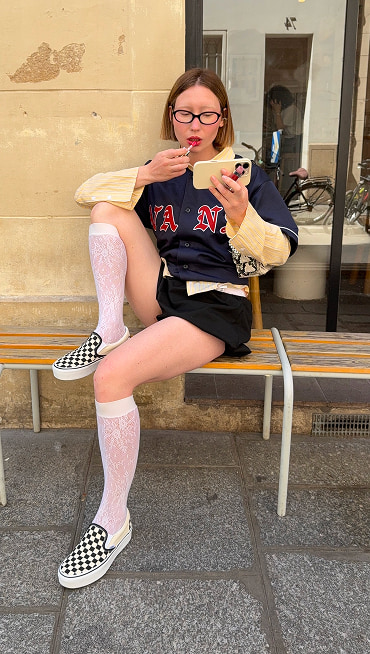 Influencer @volgaleoni does her makeup outside of a coffee shop wearing knee-high socks and black and white Checkerboard Classic Slip-On.