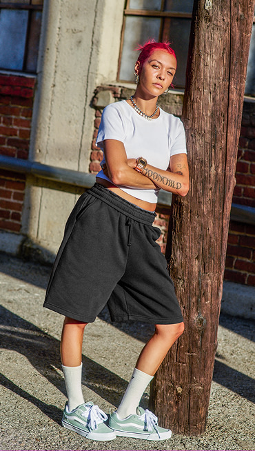 A woman with vibrant red-dyed hair leans up against a telephone pole outside a warehouse wearing white Vans crew socks and mint green Knu Skool.