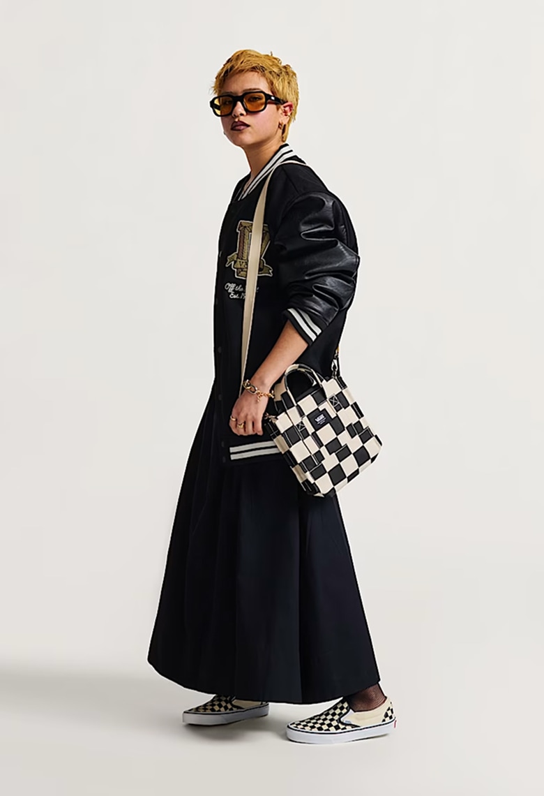 A woman poses in a photography studio wearing a black varsity-style jacket, black skirt, and a black and white Lil Pergs Tote Bag.
