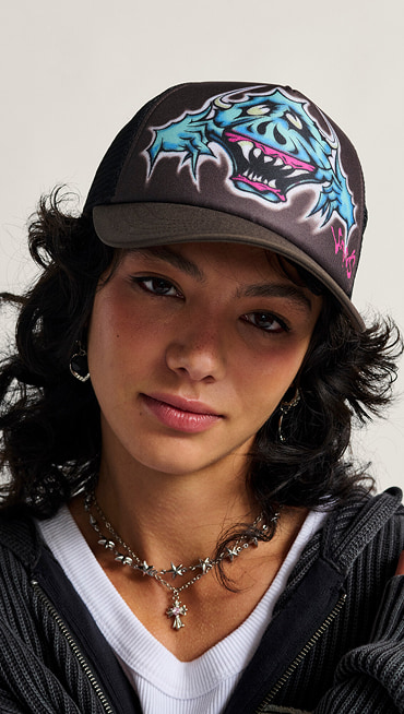 A woman looks into the camera wearing a Vans trucker hat and a silver necklace.