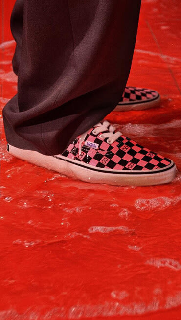 A close-up of the pink and black checkerboard pattern on the Authentic by Valentino Garavani and Vans in a red room.