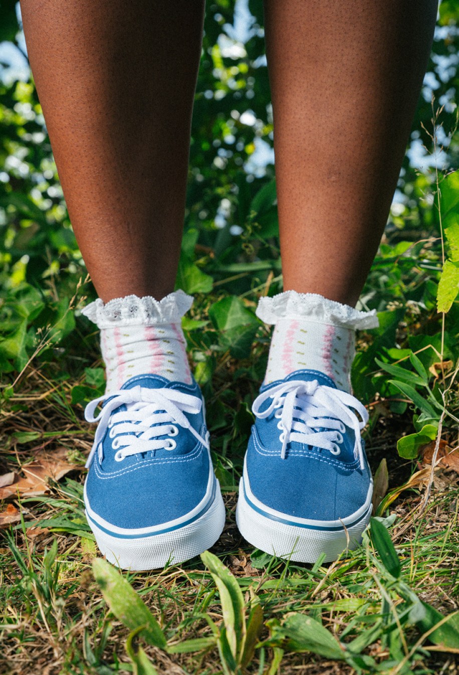 A close-up of someone wearing blue Authentic with frill socks on some grass on a sunny day.