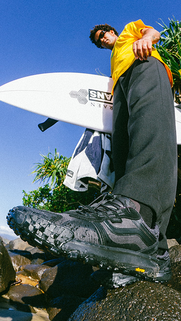 A ground-up shot of Vans Surf Team Rider Mikey February holding a surfboard wearing black Crosspath XC GORE-TEX.