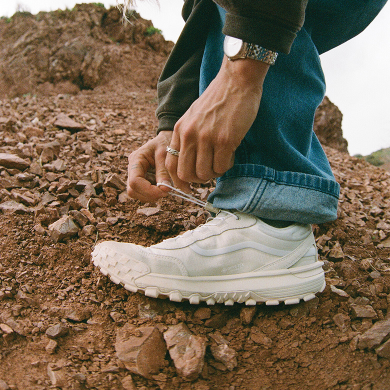 A knee-down shot of someone wearing the white Crosspath XC GORE-TEX with blue jeans standing on red rocks.