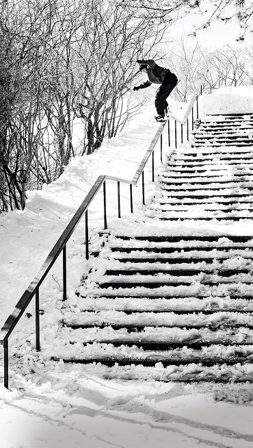 Vans Snowboard Team Rider Ivika Jürgenson grinds the rail of a snowy staircase in a black and white photo.