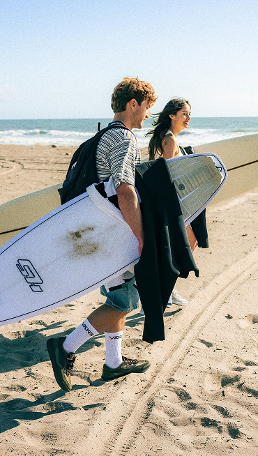 Vans Surf team riders Micky Clarke and Maddie Miller walk down the beach holding surfboards and wearing the UltraRange 2.0.