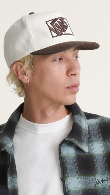 A close-up of a young man wearing the Crestmon Plaid Shacket and a white Vans logo hat.