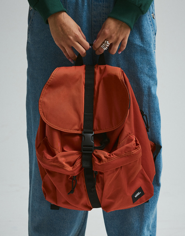 A waist-down shot of someone holding an orange backpack in a photography studio.