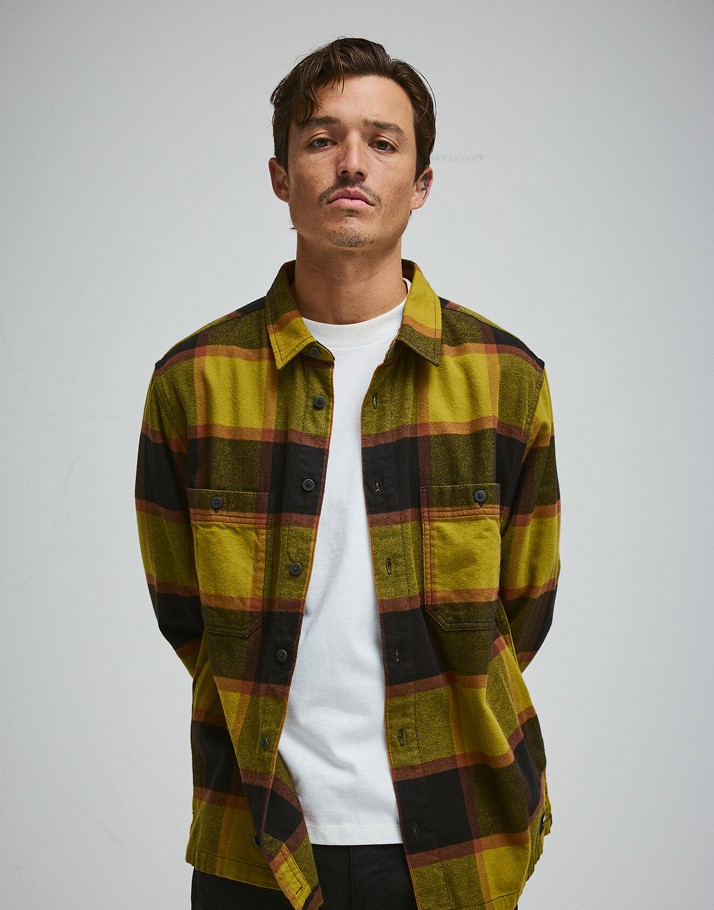 A man poses in a photography studio wearing a yellow Larkspur Plaid Flannel Shirt.