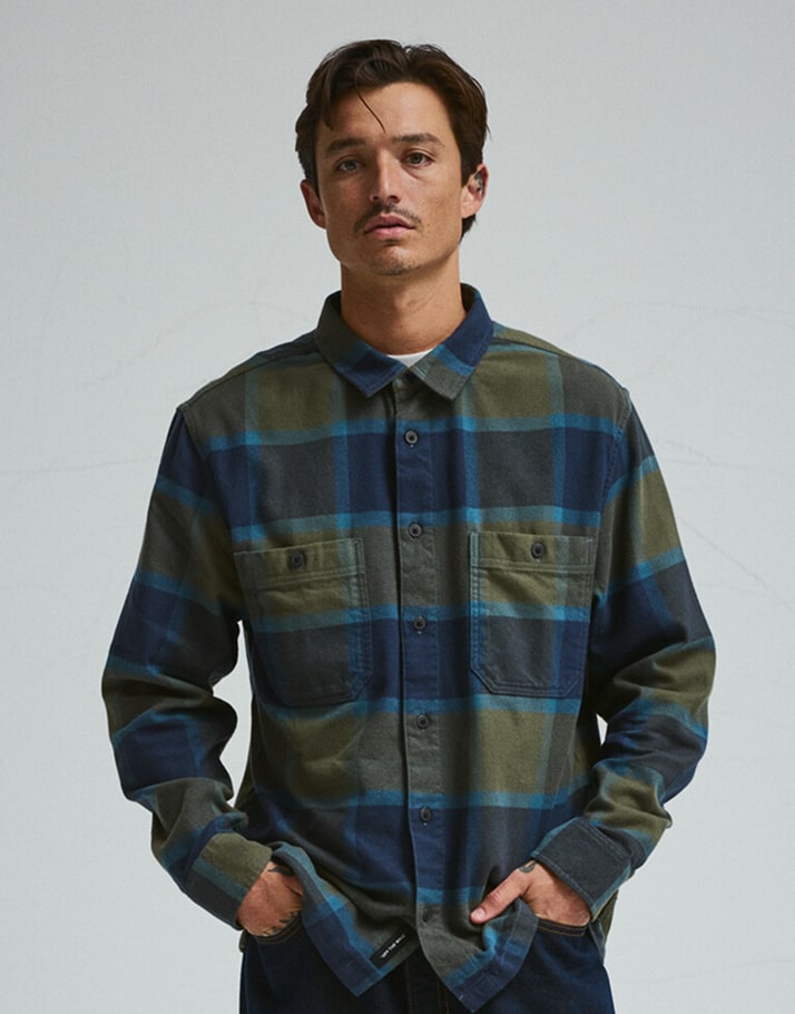 A young man poses in a green and blue Larkspur Plaid Flannel Shirt in a photography studio.