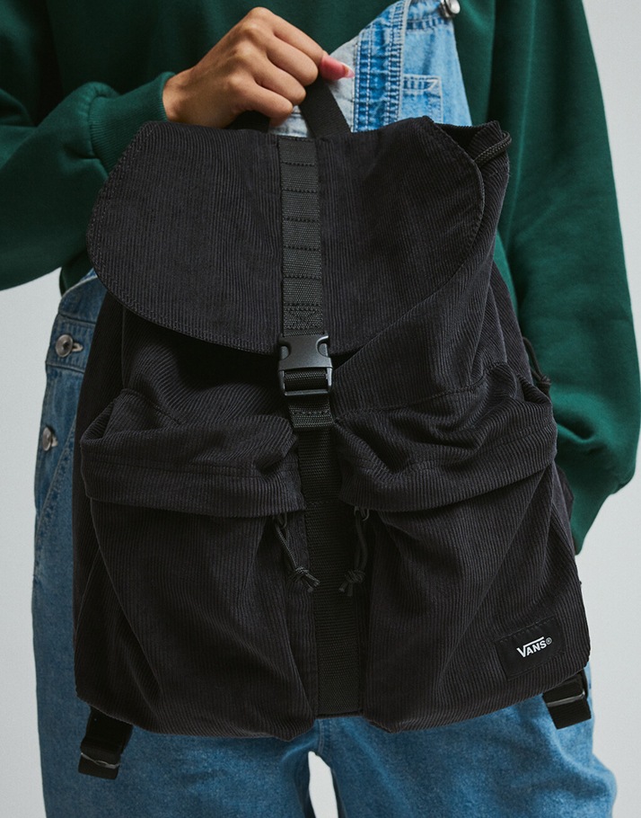 A close-up of someone holding the black Scatter Backpack against the blue denim Sirelle overalls in a photography studio.