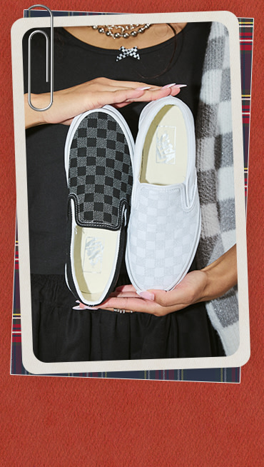 A young woman holding up two different bedazzled Checkerboard Classic Slip-On glinting in the light.