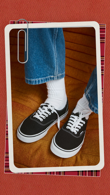 Close-up of someone wearing black Authentic with blue jeans and white Vans crew socks on an orange sofa.