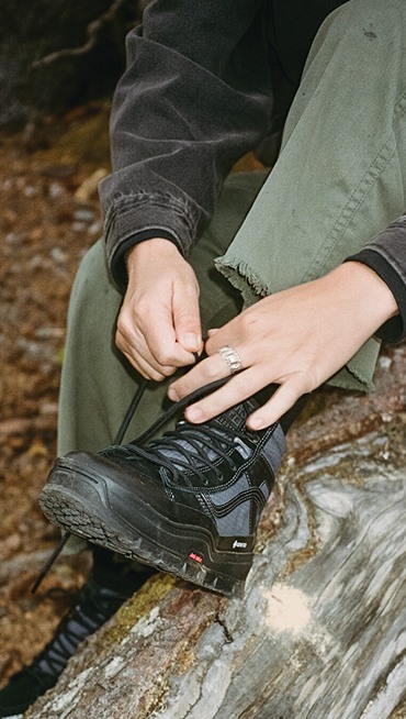 Someone laces up the black Sk8-Hi GORE-TEX on a log out in the woods.