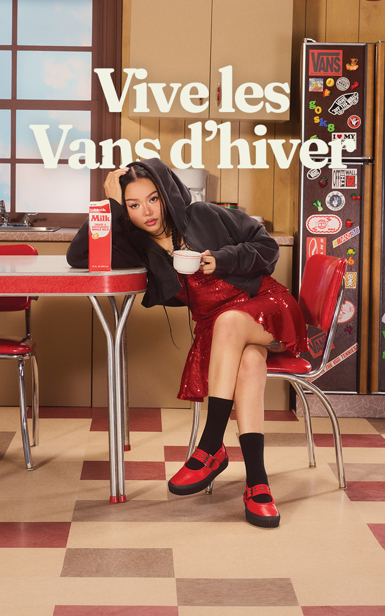 L’influenceuse Bella Poarch est assise à une table de cuisine, portant les Mary Jane Creeper rouge vif, à côté d’un carton de lait sur un plateau de sitcom.