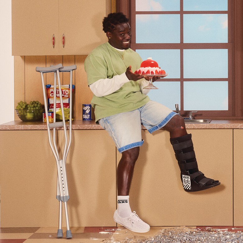 Vans Skate Team Rider Zion Wright sits on the kitchen counter of a sitcom set holding a fruit cake.