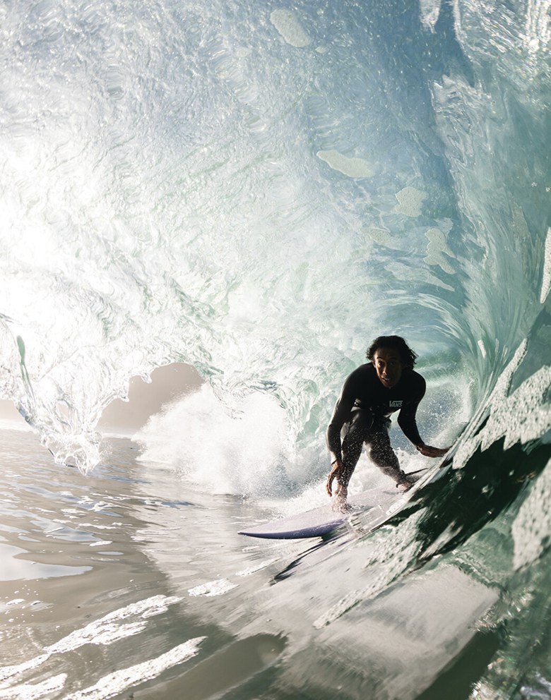 A Vans athlete and professional surfer rides a wave inside a barrel towards the camera.