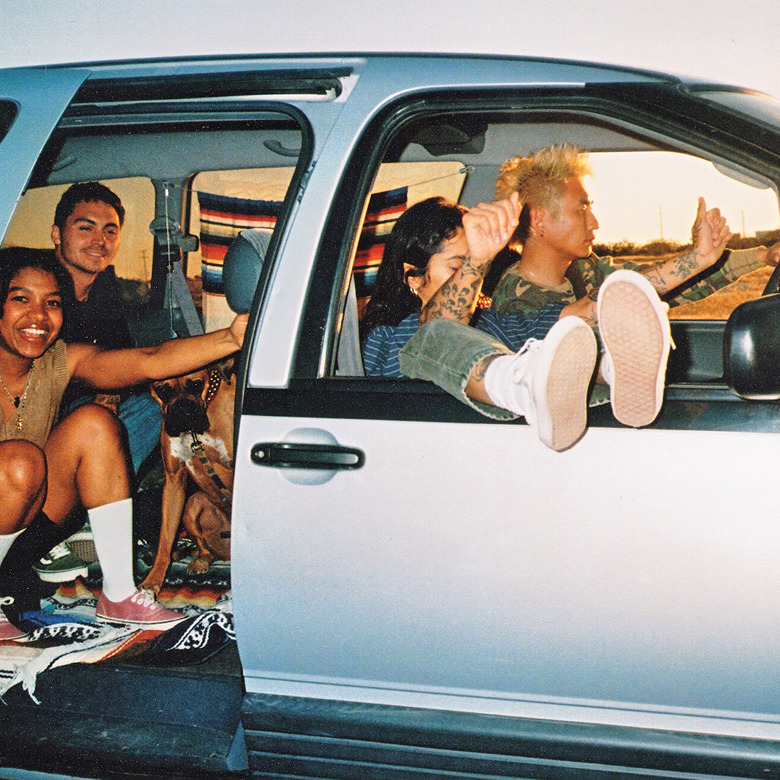 A minivan of four people and a dog, the two people in front dancing to music as the two in the back smile and shut the door.