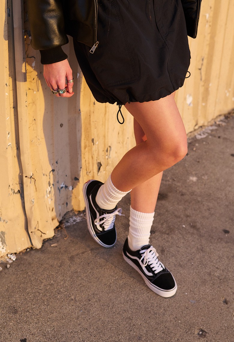 A pair of black and white Old Skool paired with white socks on a person standing on the beach.