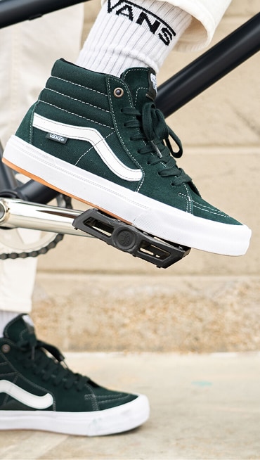 Close-up shot of a person wearing Dark Forest BMX Sk8-Hi shoes and white socks with a Vans logo.