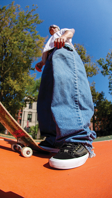 A person standing with baggy jeans and skateboard.