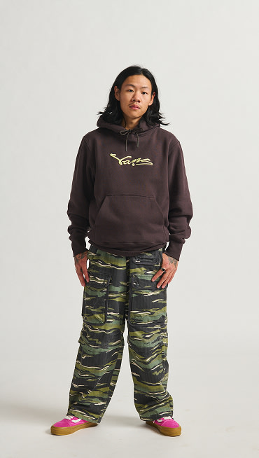 A man standing in baggy green cargo pants and a hoodie.