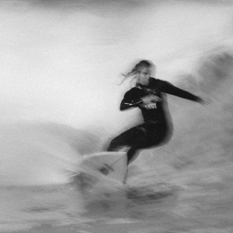 A black and white blurry image of a surfer carving on a wave.