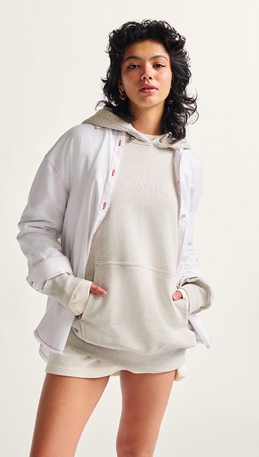 A woman poses and looks into the camera in a Vans Premium Logo Hoodie under a white Gillian Button Up Shirt.