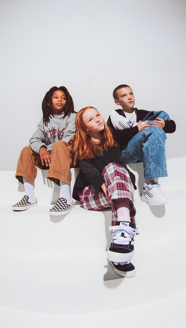 Three kids sitting together wearing Vans clothes, Classic Slip-On Checkerboard Shoe, Knu Skool, and Hylane.