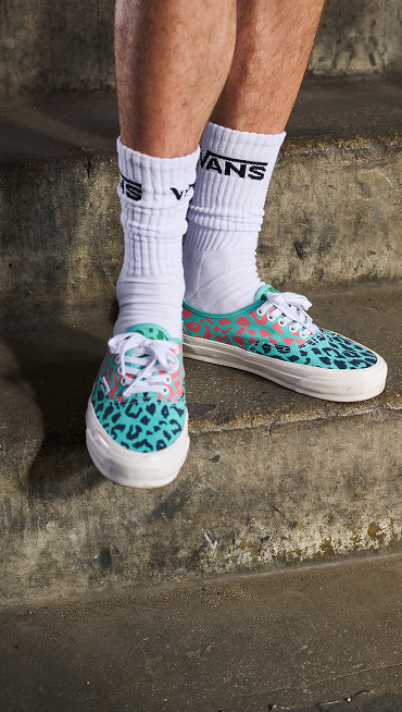 Somebody on concrete stairs wearing the Premium Authentic in Cheetah Pool Blue paired with white quarter socks with the Vans logo.
