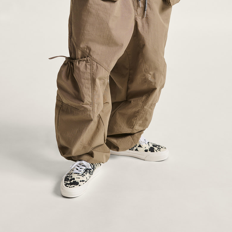 A waist-down shot of a woman wearing baggy pants and black and white spotted Premium Authentic shoes.